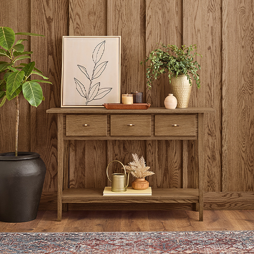 Stained wainscoting behind a side table with artwork and plants.