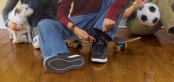 hardwood floor with person putting on shoes, skateboard and a small dog